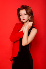 Attractive, young woman in a black dress and a red jacket, posing while standing against a red background.