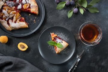 Tasty fall pie galette with plum and apricot on black table.