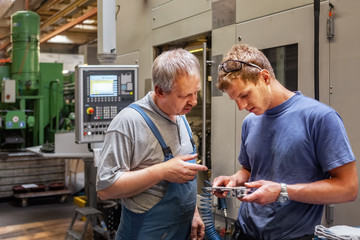 Skilled workers standing in a production hall in front of a machine tool, checking a workpiece