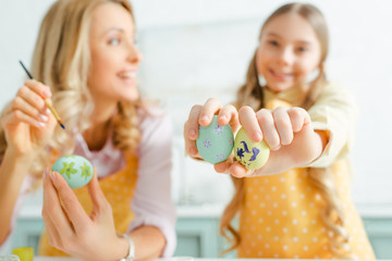 selective focus of happy kid holding painted easter eggs near mother