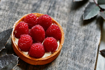 Tartlet with raspberries. Dessert on the dark board. Decoration of dessert with leaflets.