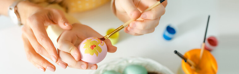 panoramic shot of kid painting easter egg near mother on white
