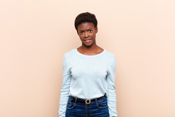 young pretty black womanlooking puzzled and confused, biting lip with a nervous gesture, not...