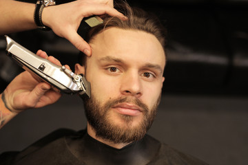A new look. Close up shot of a serious man who is having his beard trimmed with a professional electric shaver in a barbershop.