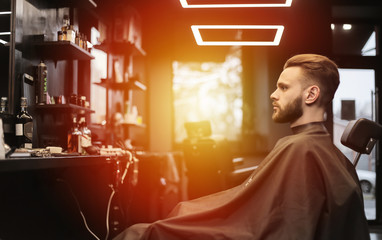 Man in barber shop. Young handsome man is looking at his reflection in the mirror while waiting for a professional barber to take care of his hair.