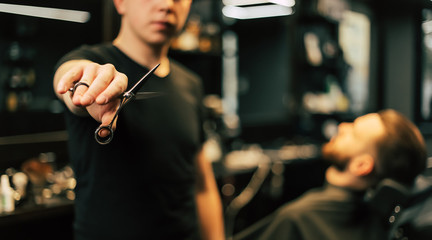 Ready to style him up. Close-up photo of a young barber in a black t-shirt who is holding scissors in his right hand stretched towards the camera.