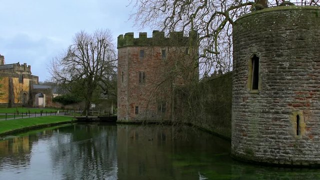 Over the moat, looking towards the imposing walls and castle towers of the Medieval Bishop's Palace in Well, UK