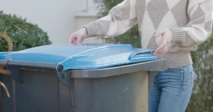 Woman opens blue paper bin in slow motion. The garbage can is full of waste, mainly packaging material from online / mail orders.