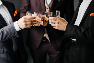 Close-up partial view of three friends clink glasses of whiskey drink, alcoholic beverage. Whisky drink