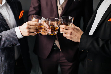 Close-up partial view of three friends clink glasses of whiskey drink, alcoholic beverage. Whisky drink