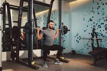Young handsome man doing squat exercises at the gym on a squat machine