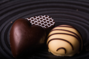  Three delicious chocolate bonbons on a black plate. Horizontal format