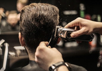 Men style. Close up photo of a barber’s hands working with electric shaver and comb to make a new...