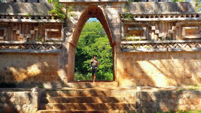 Aerial, drone shot over a man walking through a gate at the Labna ruins, sunny day, in Yucatan, Mexico