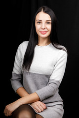 Portrait of serious beautiful female with black hair, has minimal makeup, looks calmly at camera, wears white jumper, stands against black background, being deep in thoughts