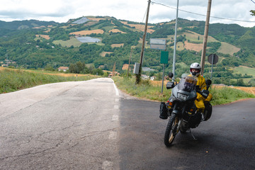 Motorcyclist traveler girl wearing yellow raincoat and sitting in a motorcycle saddle. Motorbike on mountain road. Extreme travel tour. Biker equipment. Copy space.