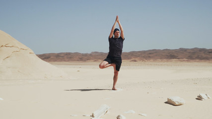 Fototapeta na wymiar Handsome male doing yoga tree pose vrikshasana on a rock in desert