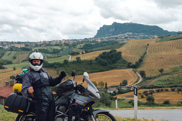A motorcycle traveler arrived at his destination and he feels happiness. San Marino mountain on...