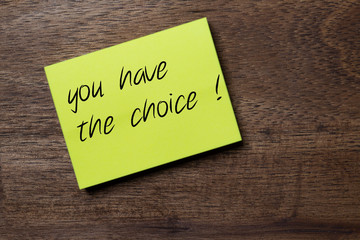yellow sticker on a dark wooden background with the handwriting phrase to encourage a decision: you have the choice