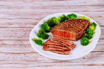Sliced rare beef tenderloin with broccoli on white plate.