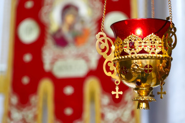 Orthodox Church Church lamp with a lit candle and red glass in a gold case hangs in front of icons