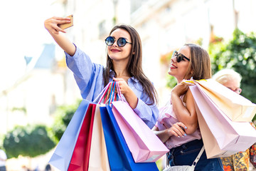 Inspired women are using smartphone vlogging their shopping day on blurred city background.