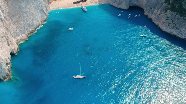 Saling boats floating in the crystal clear turquoise water. Sandy beach secluded by sheer white cliffs with the shipwreck as a touristic attraction. Aerial tilting establishing shot