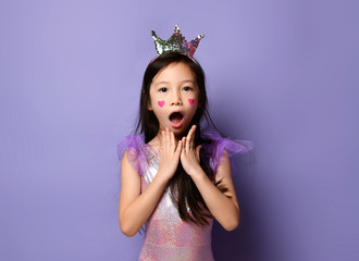 Portrait of surprised asian korean kid girl princess in party dress and crown and with painted red hearts sign on cheeks