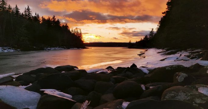 Sunset at the mouth of a Beautiful rocky and snow covered cove surrounded by dead fall pine trees in rural Nova Scotia, Canada