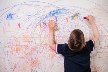 The child draws on the wall with a crayon. The boy is engaged in creativity at home