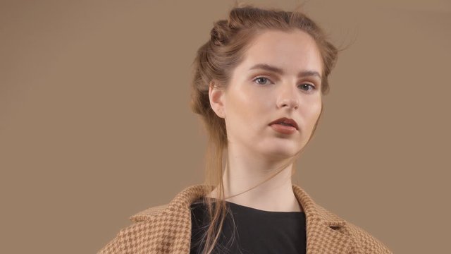 Slow motion portrait of young model with blowing hair in studio fashion portrait wears an oversized vintage jacket on brown bakcground