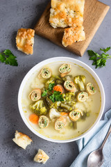 Soup with vegetables and egg pancakes in a white plate, light grey background. Traditional German Flaedlesuppe and Austrian Frittatensuppe. 