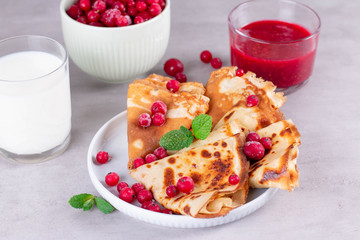 Thin pancakes or crepes on a ceramic plate with jam and frozen berries, mint