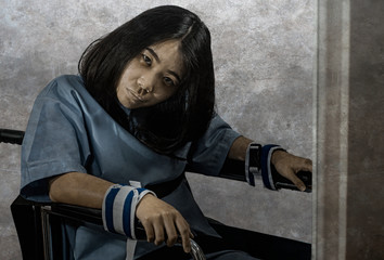 young crazy and mentally insane Asian woman restrained in wheelchair at mental hospital suffering...