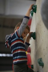 Little boy with blonde hair and striped shirt is climbing, bouldering in an indoor boulder hall          