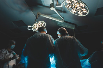 An international professional team of surgeon, assistants and anesthesiologist perform a complex operation on a patient under general anesthesia. Dark atmospheric photography theme in low key.