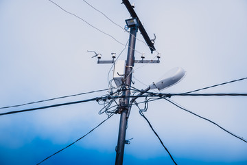 Tensioned electrical wires on high pole against the blue sky.