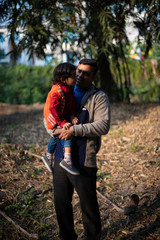 An Indian brunette father and his baby boy in winter garments enjoying themselves in winter afternoon on a  dry grass field in forest background. Indian lifestyle and parenthood.
