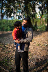 An Indian brunette father and his baby boy in winter garments enjoying themselves in winter afternoon on a  dry grass field in forest background. Indian lifestyle and parenthood.