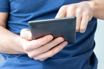 Gray e-reader electronic book in male hands. A man in a blue t-shirt with a tablet. Selective focus