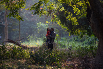 Naklejka premium An Indian Telugu brunette father and his baby boy in winter garments enjoying themselves in winter afternoon on a green grass field in forest background. Indian lifestyle and back light photography.