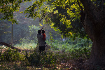 An Indian Telugu brunette father and his baby boy in winter garments enjoying themselves in winter afternoon on a  green grass field in forest background. Indian lifestyle and back light photography.