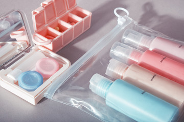 Travel kit. Set of four small plastic bottles for cosmetic products in transparent bag, kit for contact lenses, pill organizer. Gray background with shadows.