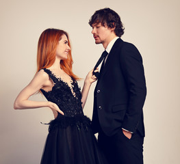 Beautiful happy couple hugging on blue background in evening fashion clothing. Redheaded hairstyle laughing girl holding on black suit her brunette man in studio. Closeup