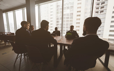 Silhouettes of people sitting at the table. A team of young businessmen working and communicating together in an office. Corporate businessteam and manager in a meeting.