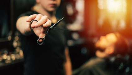 Fototapeta na wymiar Sharp blade. Close-up photo of a young hairstylist in a black t-shirt who is holding scissors in his right hand, stretched towards the camera.