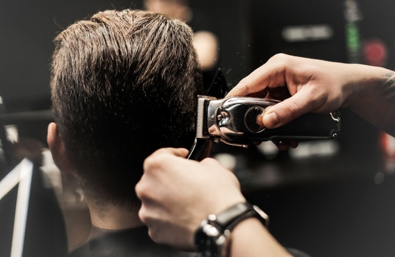 Movement of professional hands. Close up photo of a barber’s hands making a new hairstyle for a client, using a comb and electric razor.