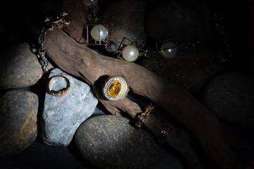 Yellow Sapphire and Diamond Ring Resting on a branch With a pearl bracelet decorated Placed on a beautiful patterned stone Along with firing the flash light To emphasize the ring to stand out