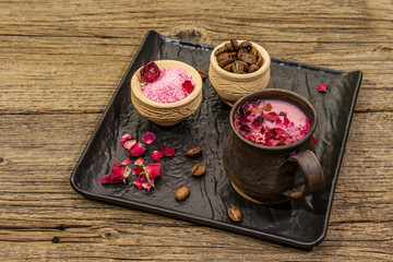 Trendy colored latte. Rose petals and powdered aromatic sugar, coffee beans. Wooden boards background