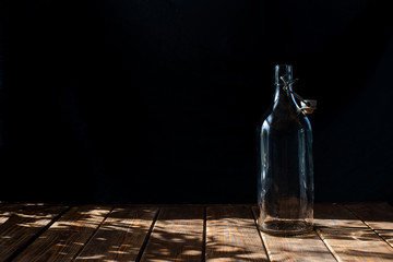 transparent glass bottle brown wooden table dark background backdrop sun glare contrast drinks wine...